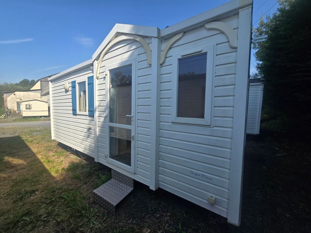 Cabine de bureau portable blanche avec garnitures bleues, porte d'entrée et fenêtres, présentée à l'extérieur sur l'herbe.