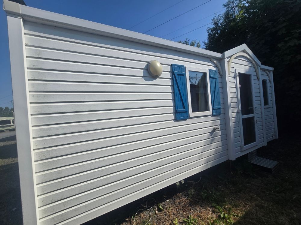 Maison mobile blanche avec des volets bleus et une petite véranda sous un ciel dégagé