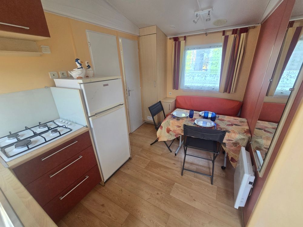 Petite cuisine avec réfrigérateur, cuisinière, table, chaises et une fenêtre laissant entrer la lumière du jour.
