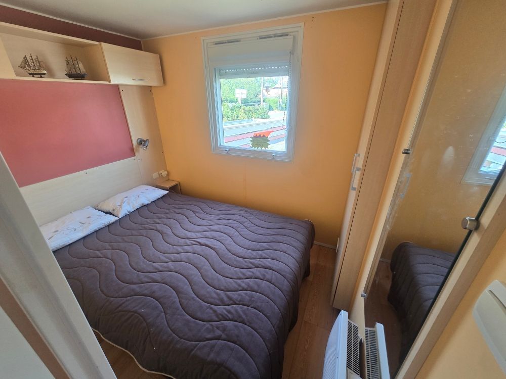 Petite chambre avec un lit, un panneau mural rose, une fenêtre et une porte de placard à miroir