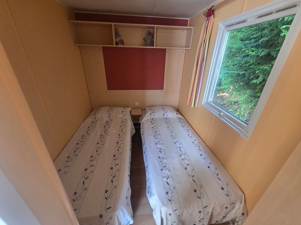 Petite chambre avec deux lits simples, une fenêtre et des étagères intégrées.