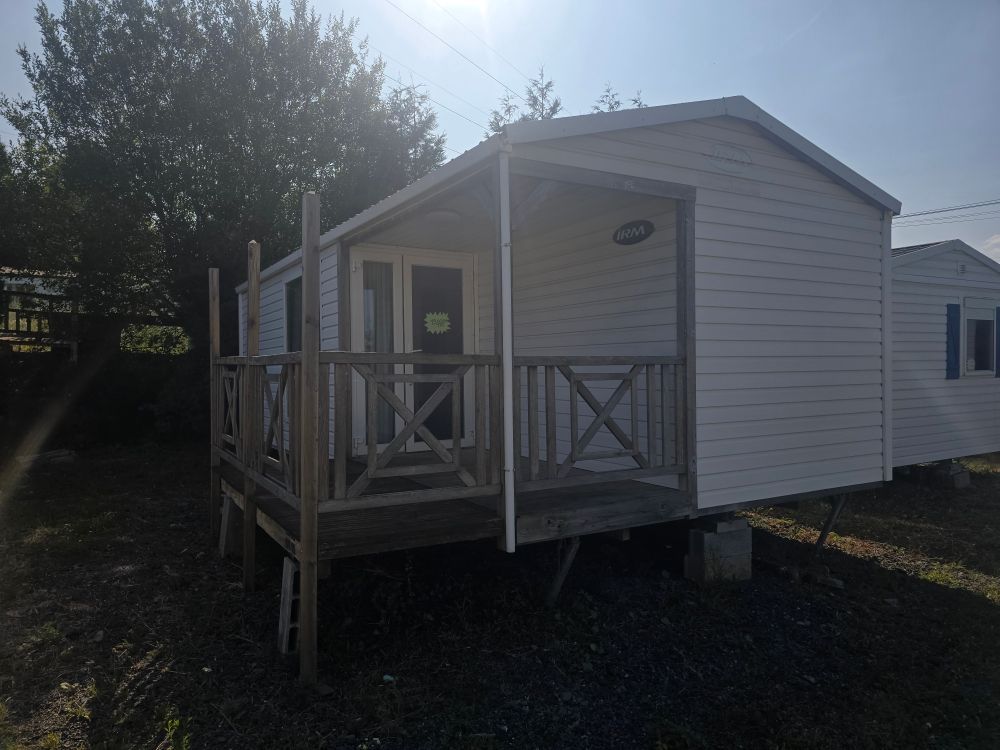 Maison mobile blanche avec un petit porche et une balustrade dans une cour ensoleillée