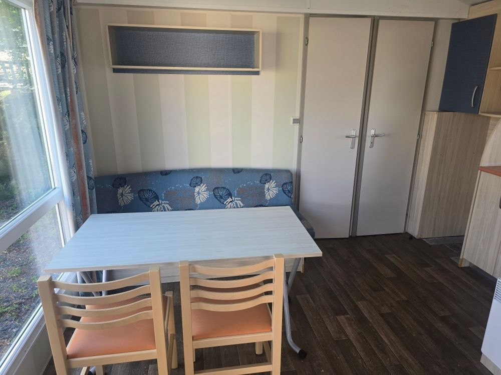 Petit coin repas avec table blanche, banc bleu, deux chaises et placards près d'une fenêtre