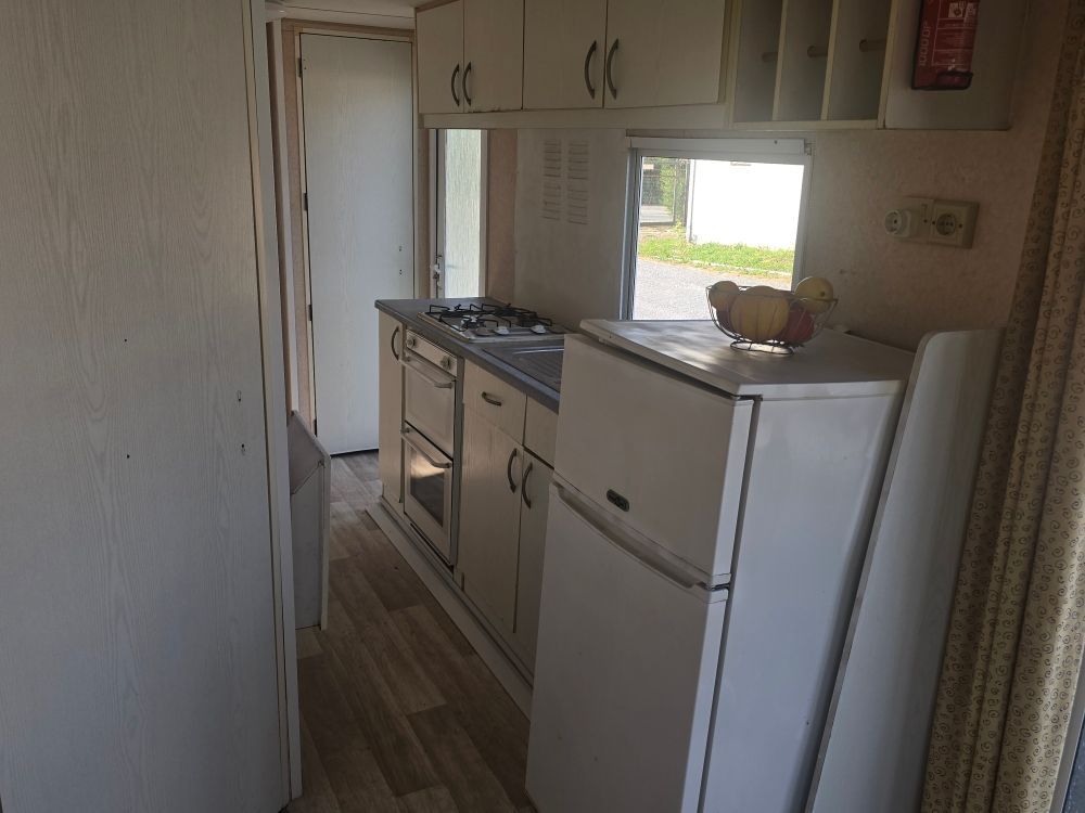Cuisine étroite avec placards blancs, cuisinière, réfrigérateur et une fenêtre lumineuse au fond.
