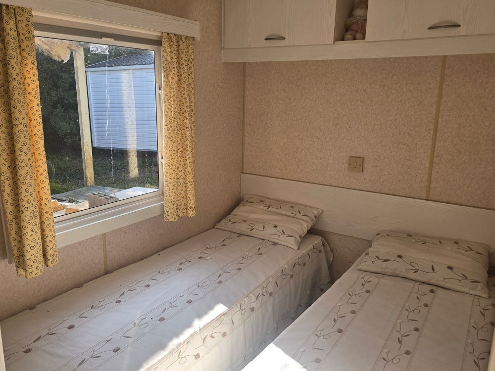 Petite chambre avec deux lits simples, une fenêtre, des rideaux et des armoires couleur crème.