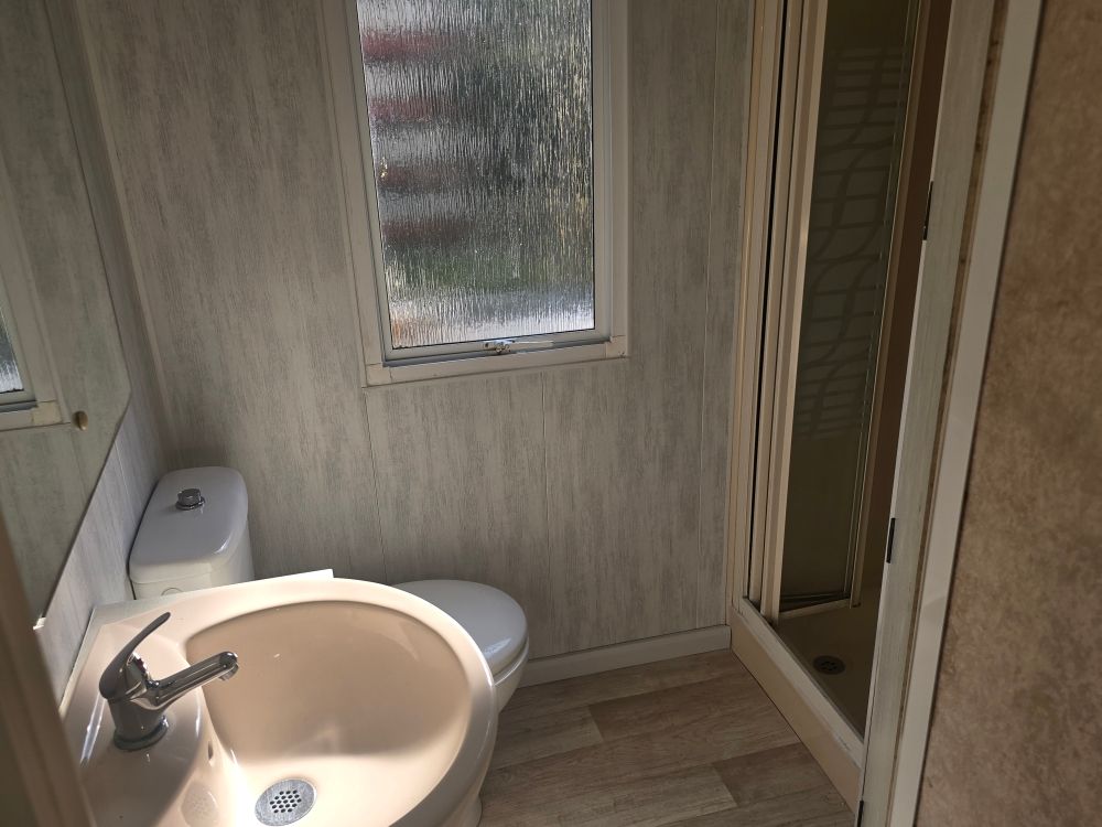Petite salle de bains avec lavabo, toilettes, fenêtre dépolie et cabine de douche dans des tons beiges.
