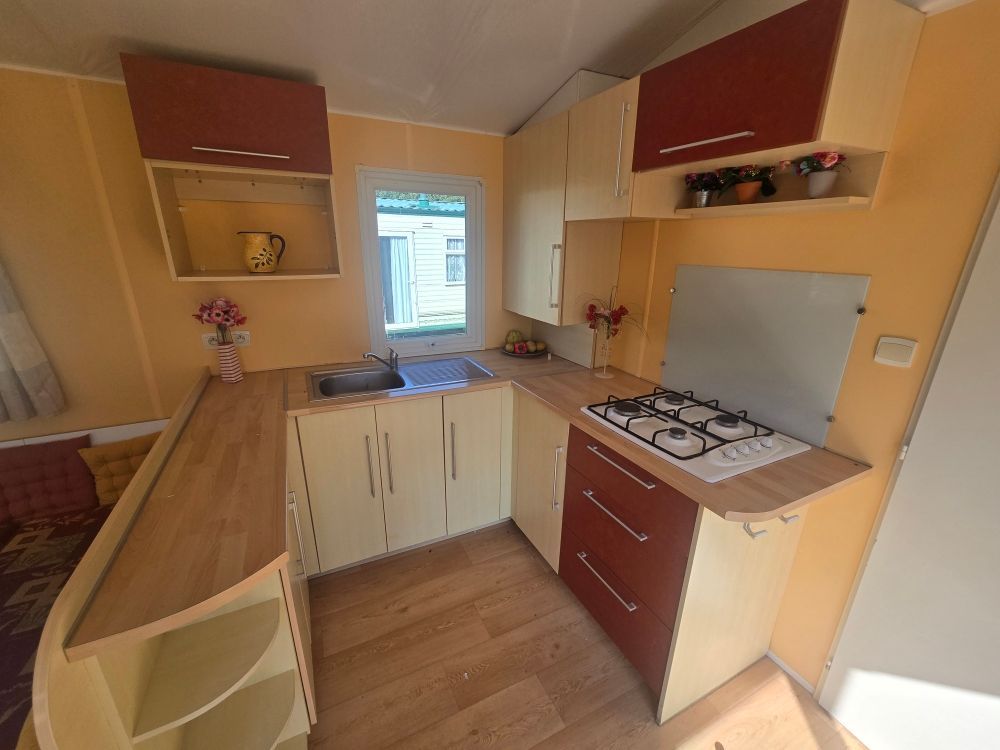 Petite cuisine avec placards beiges, plans de travail en bois et cuisinière à gaz près d'une fenêtre.