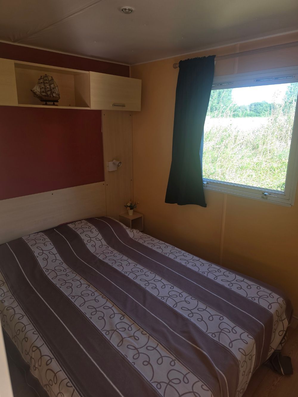 Petite chambre avec un couvre-lit à rayures, des armoires murales et une fenêtre avec des rideaux verts.