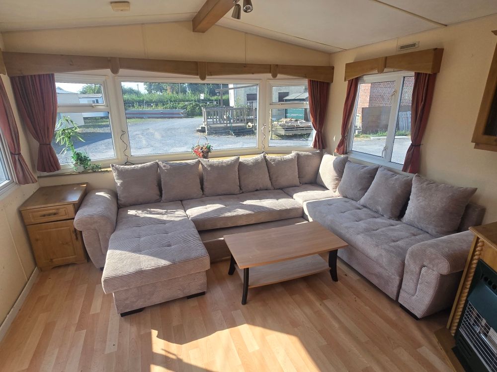 Véranda lumineuse avec canapé d'angle beige, pouf et table basse en bois donnant sur une vue sur le front de mer