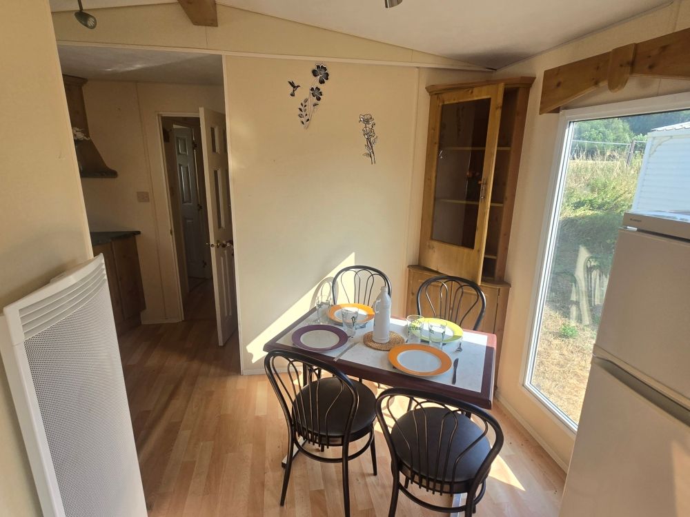 Petit coin cuisine avec une table, quatre chaises et la lumière du soleil grâce à une fenêtre et une porte ouverte.