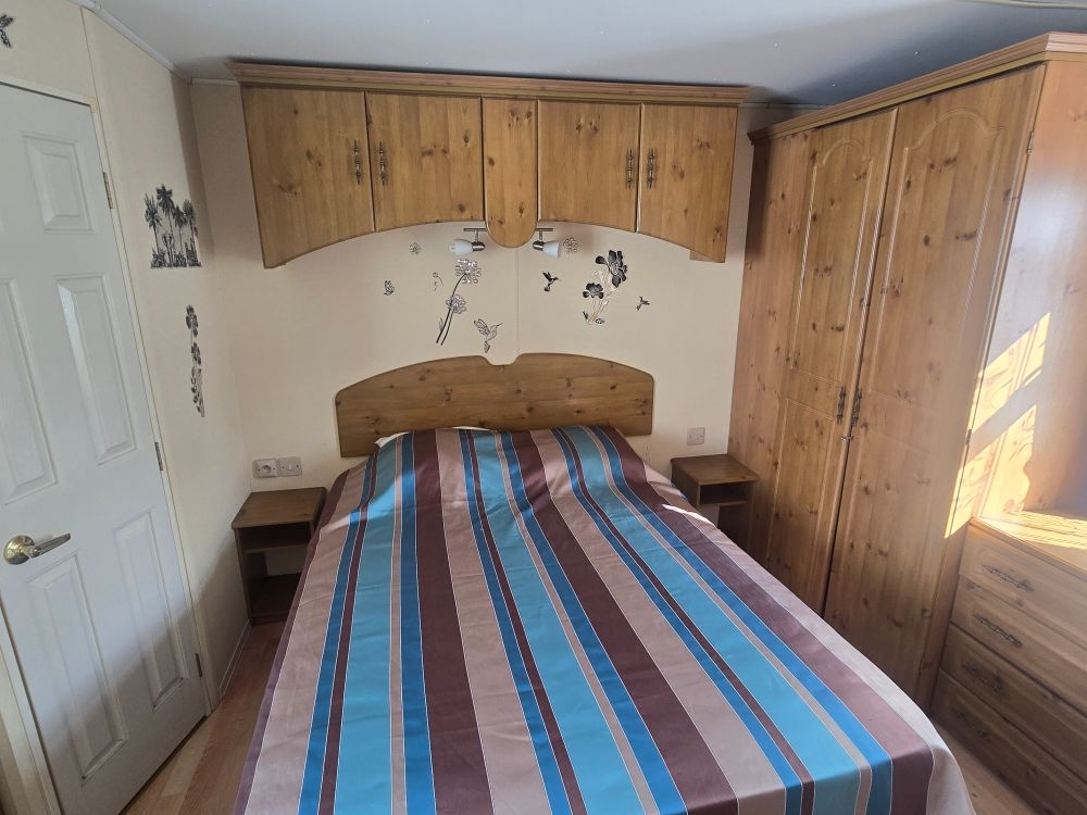 Petite chambre avec un lit simple, une couette rayée bleu et rouge, des armoires en bois et une fenêtre lumineuse.