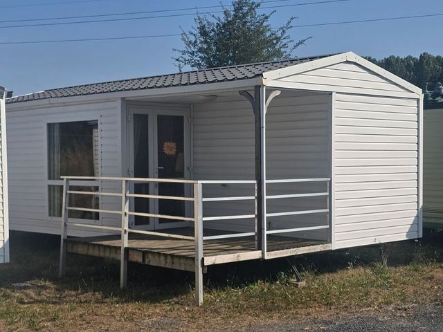 Petite maison grise avec un porche couvert et une balustrade blanche sur un terrain gazonné