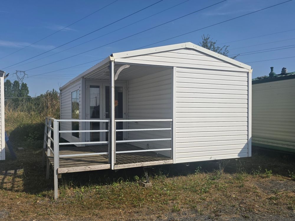 Cabane portable blanche avec un petit porche et une rampe d'accès dans un espace extérieur gazonné