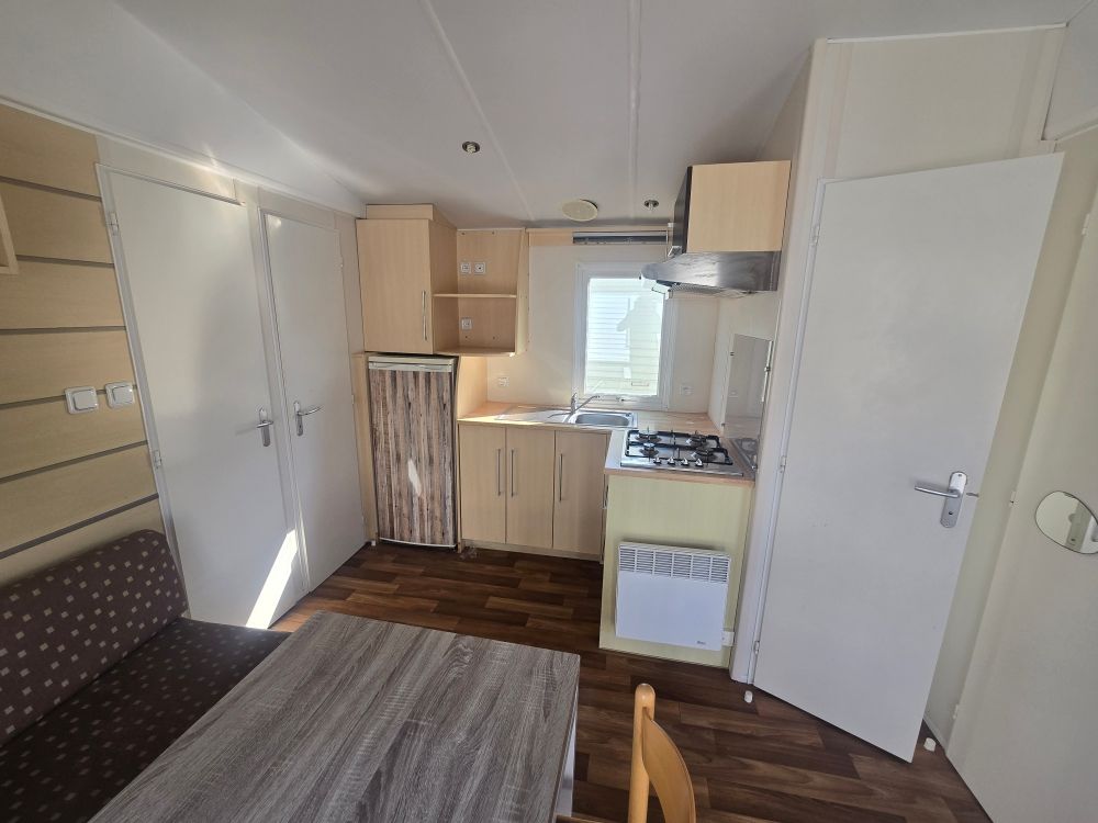 Intérieur compact et moderne d'un camping-car avec kitchenette, placards blancs, parquet et porte ouverte.