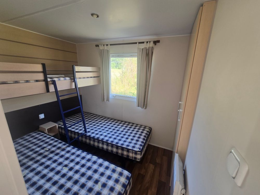 Petite chambre avec deux lits à carreaux bleus, une fenêtre et des lambris en bois clair.