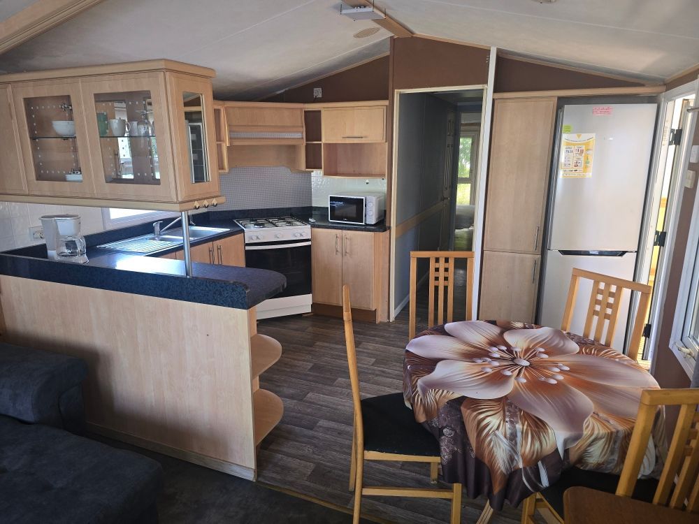 Intérieur compact de camping-car avec placards en bois, canapé et petite table à manger près de grandes fenêtres.