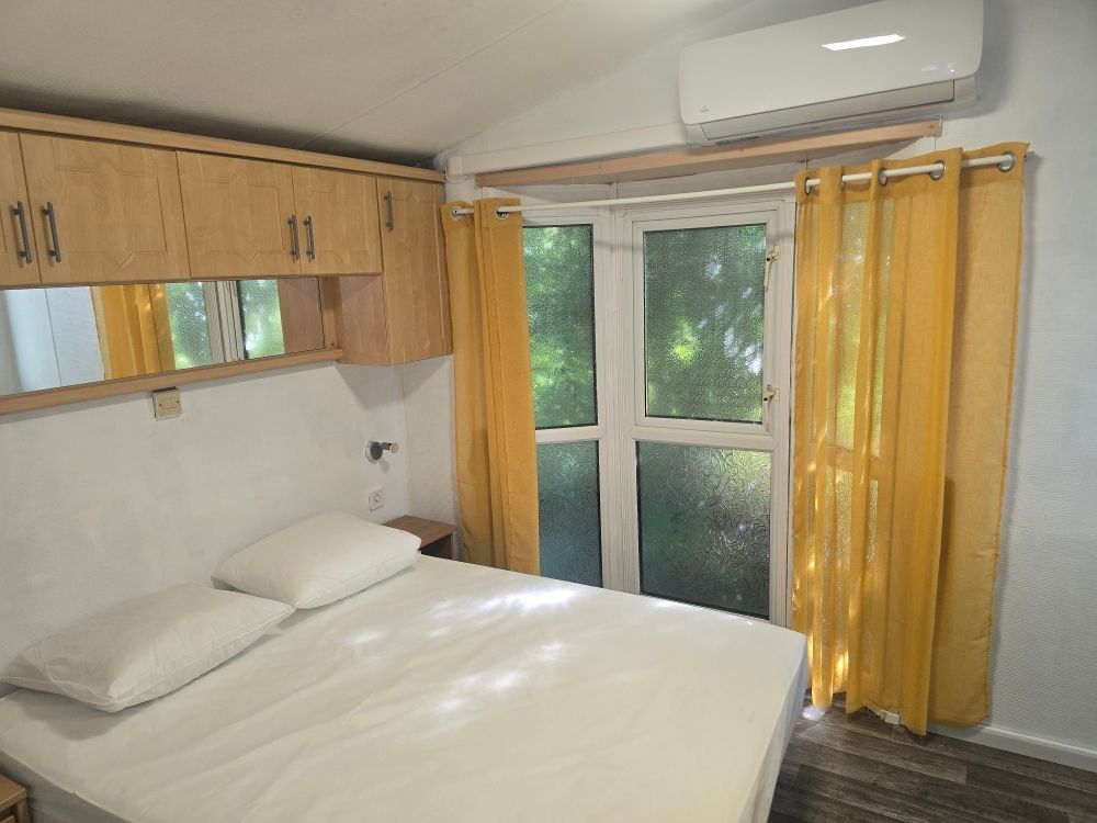 Chambre propre avec un lit, des armoires en bois et une fenêtre avec des rideaux jaunes, le tout sous un climatiseur.