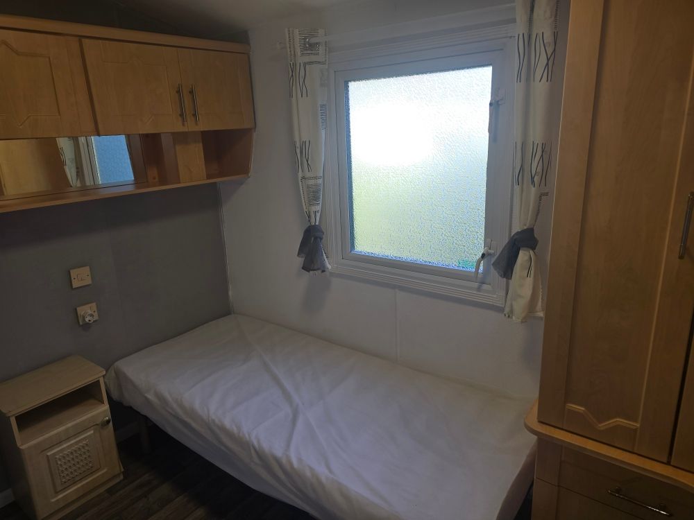 Petite chambre avec un lit simple, des armoires en bois et une fenêtre dépolie.