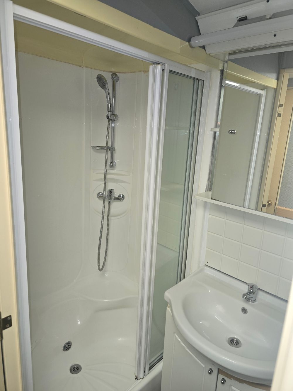Salle de bains avec cabine de douche, porte en verre et lavabo à côté d'un miroir.