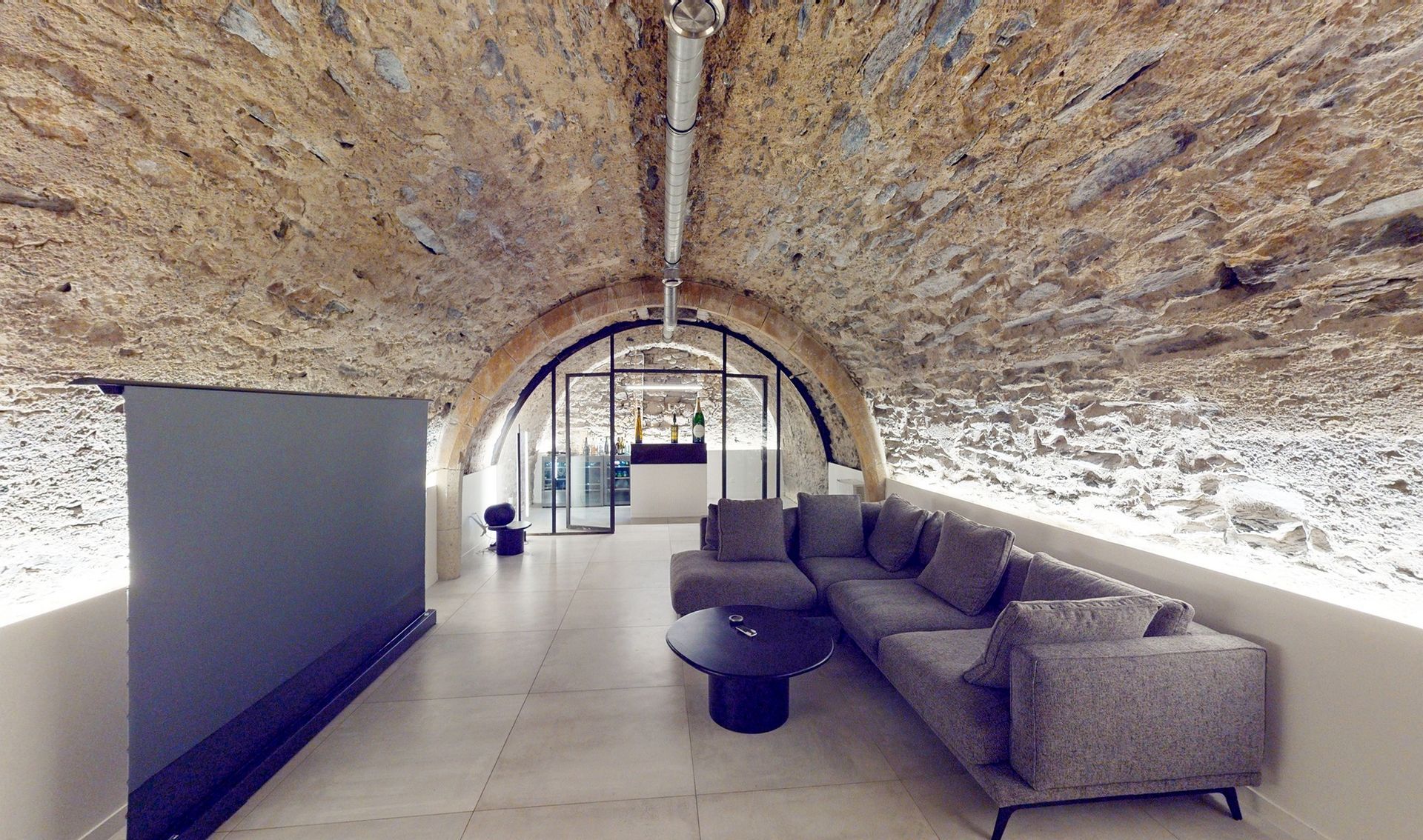 Salon dans une cave voutée en pierre avec éclairage intégré dans les murs de soubassement