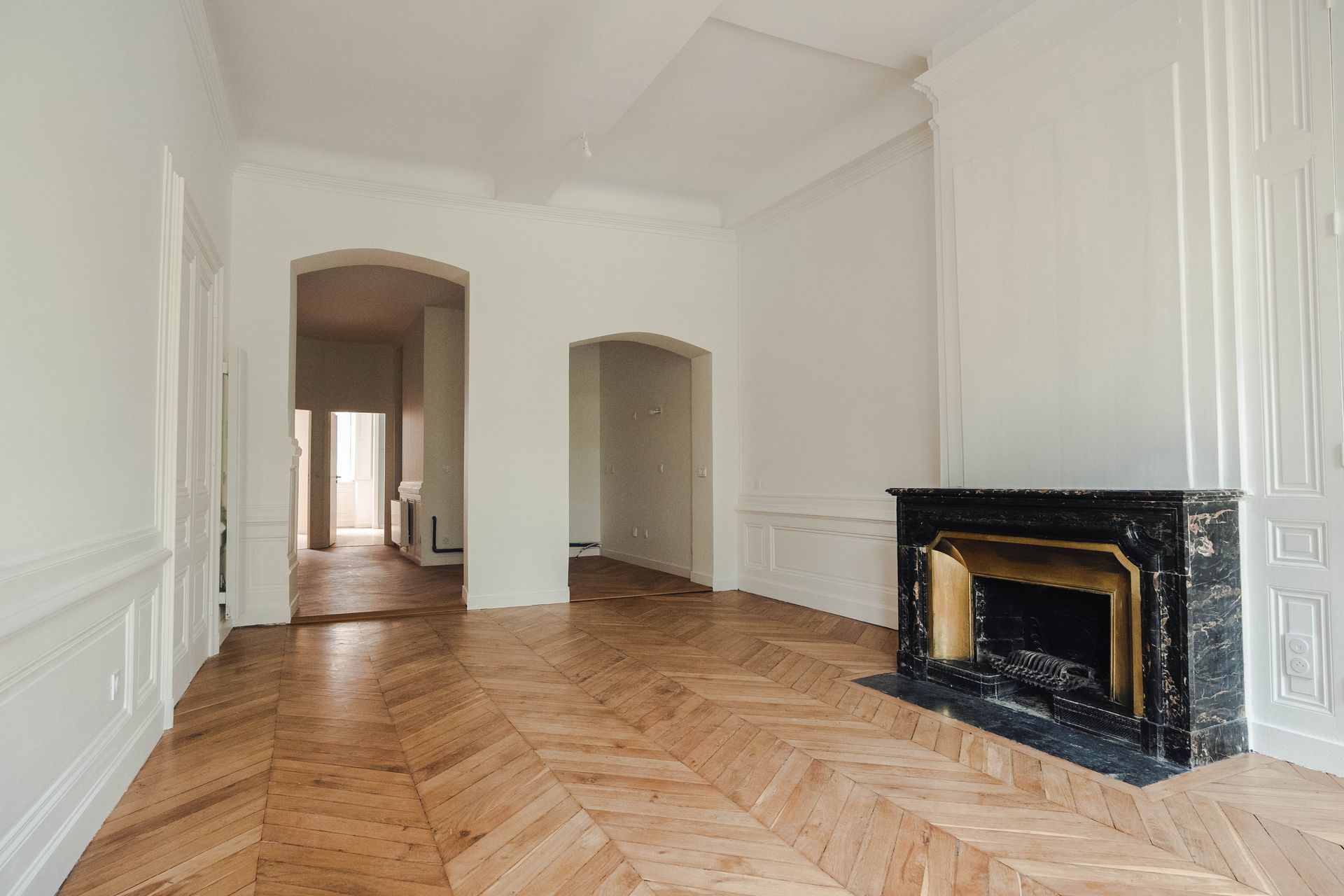 Appartement vide avec parquet chevron, cheminée en marbre et murs blancs