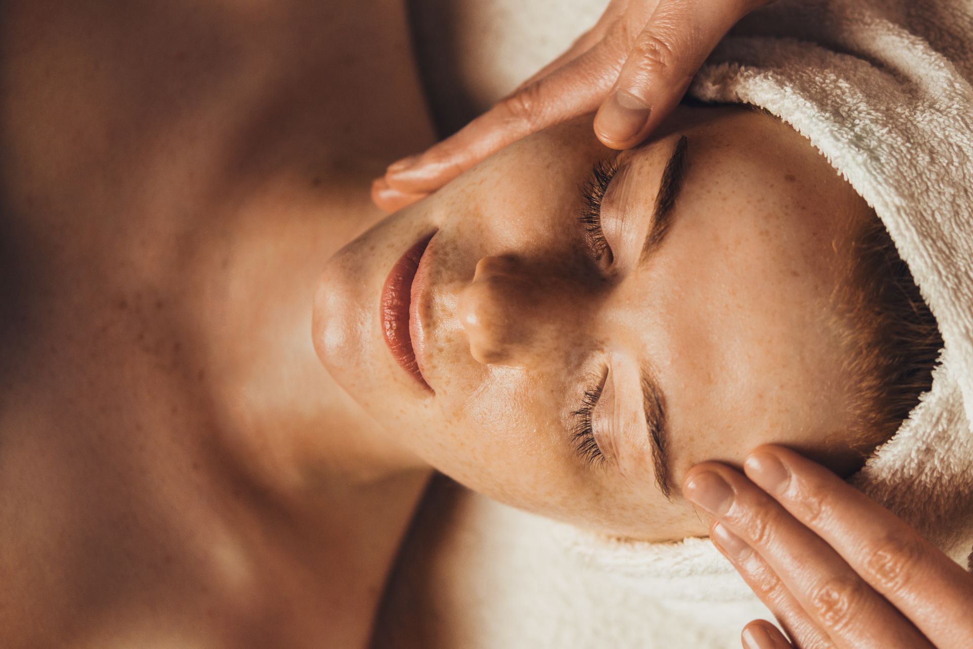 Femme recevant un massage du visage, les yeux fermés, les mains sur le visage, dans un cadre spa.