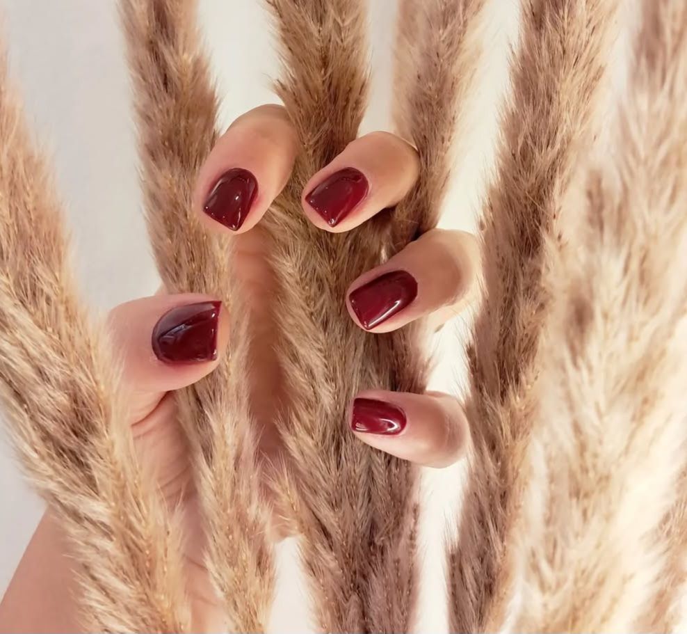 Main avec du vernis à ongles rose clair, tenant des fleurs roses.