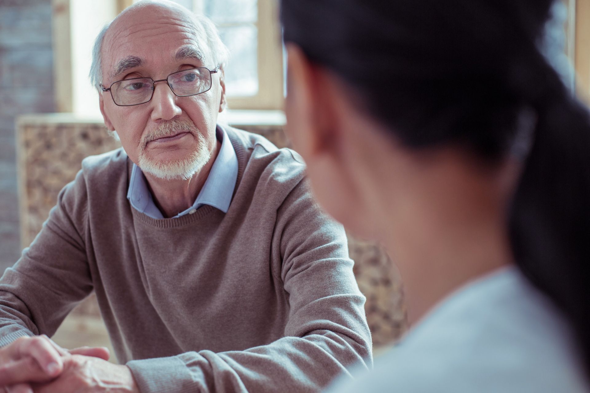 Un anciano está sentado en una mesa hablando con una enfermera.