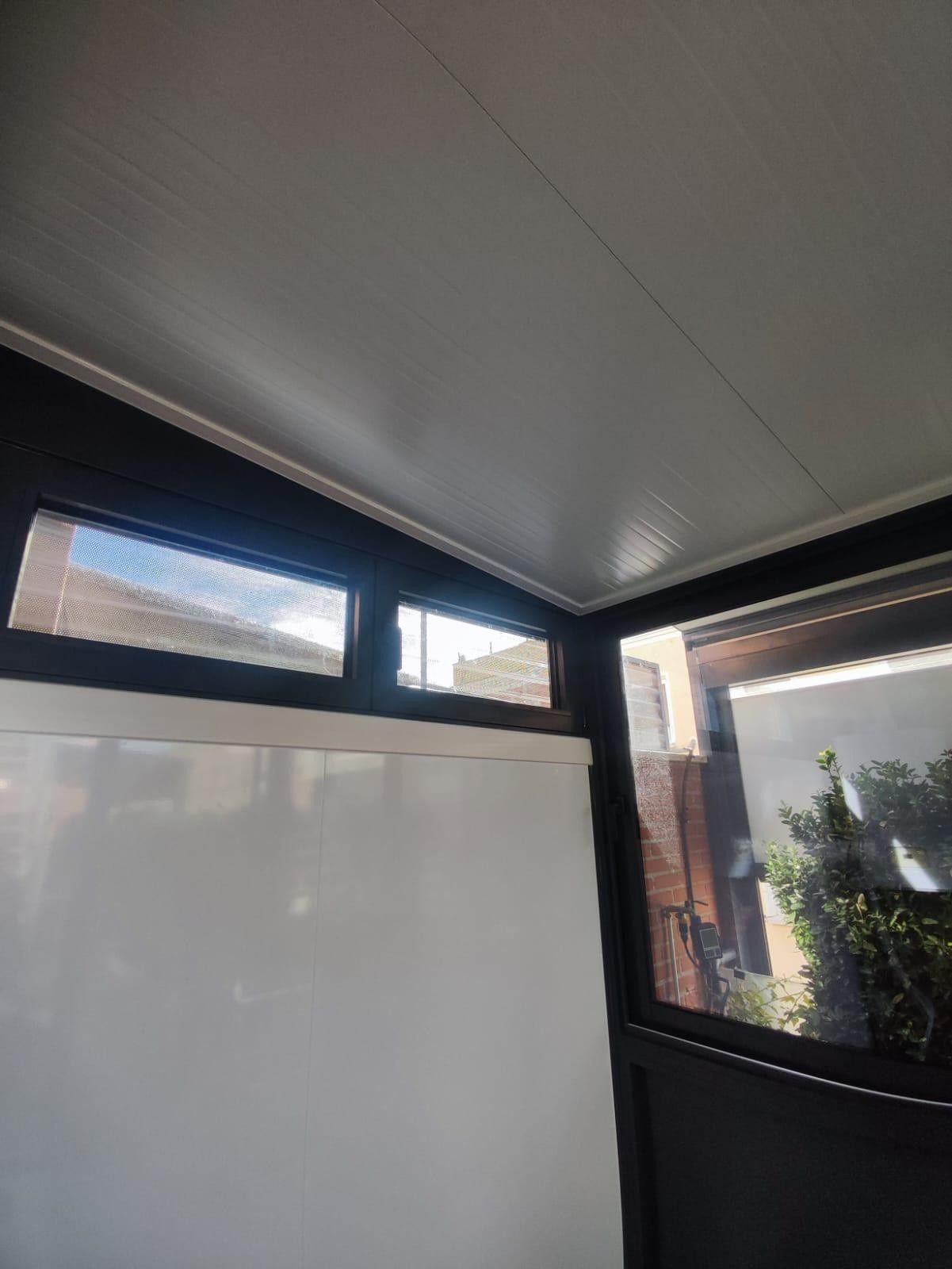 Patio cubierto con paneles de pared blancos, marco negro y pequeñas ventanas altas junto a la vegetación.