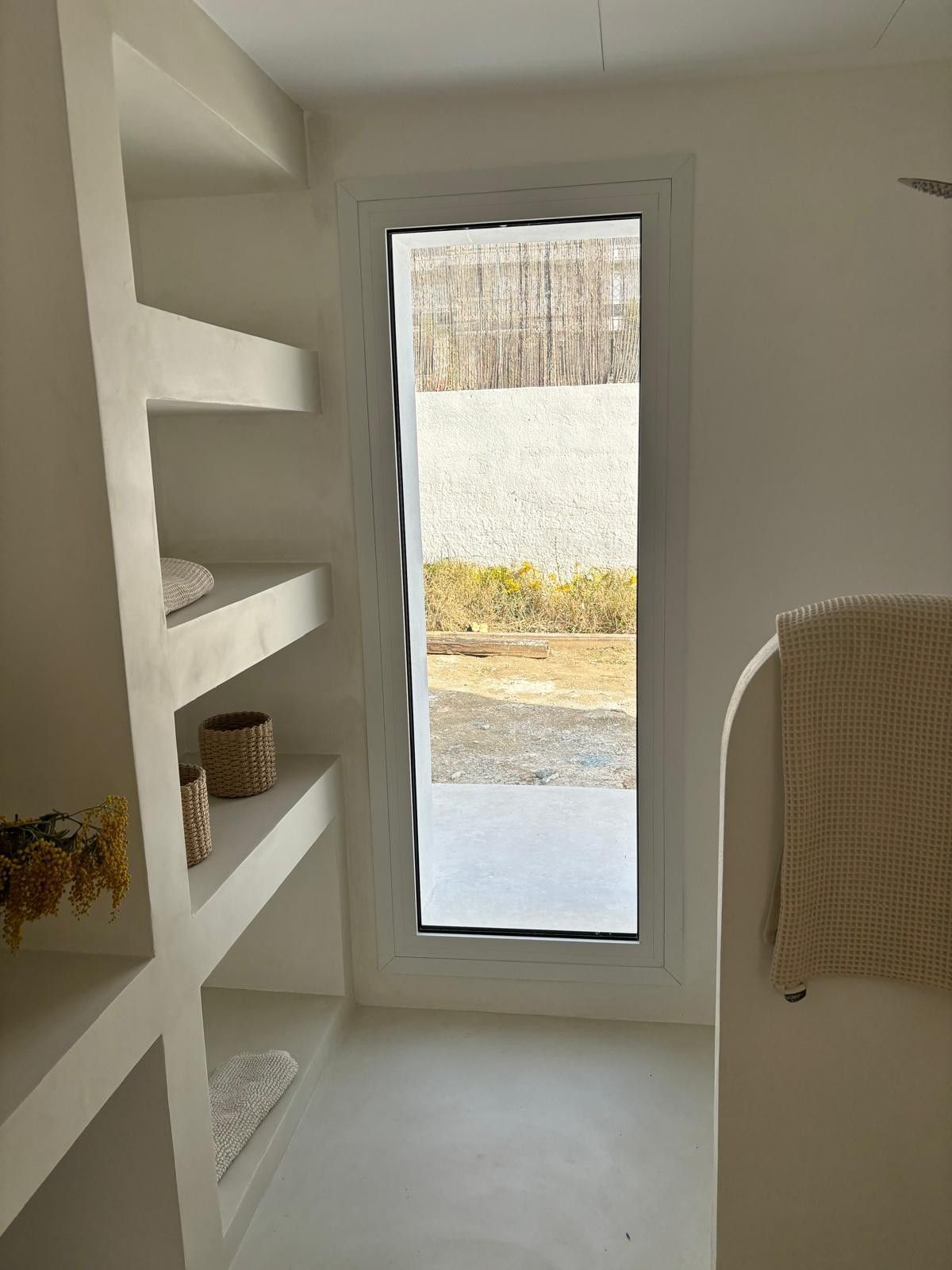 Estanterías blancas empotradas junto a una estrecha puerta de cristal que da a un patio exterior.