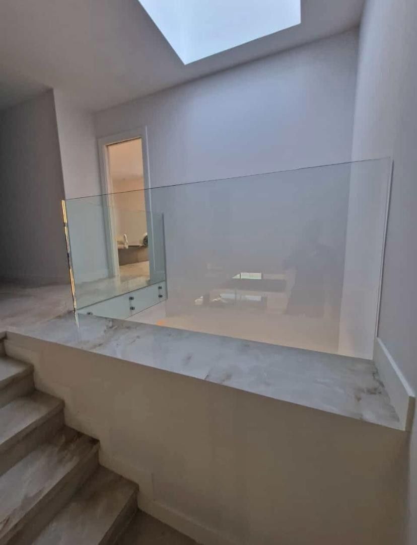 Pasillo luminoso con barandilla de cristal, escaleras y tragaluz en el techo.