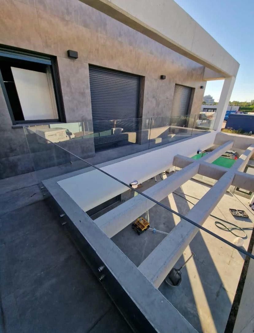 Patio moderno con barandilla de cristal, suelo gris y una mesa blanca en el exterior de un edificio beige.