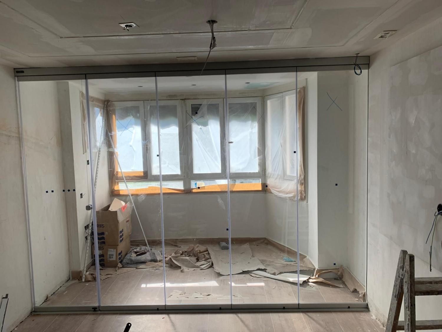 Obra en construcción con láminas de plástico alrededor de un hueco con ventana y escombros en el suelo.