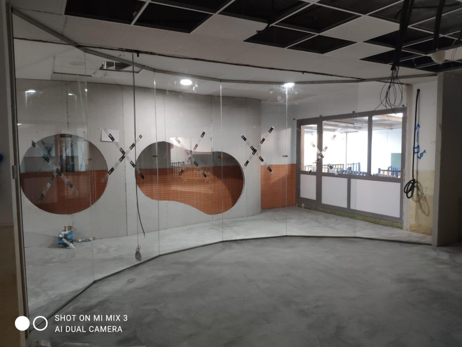 Interior de oficina vacío con suelo de hormigón, techo sin terminar y grandes aberturas de cristal en la pared.