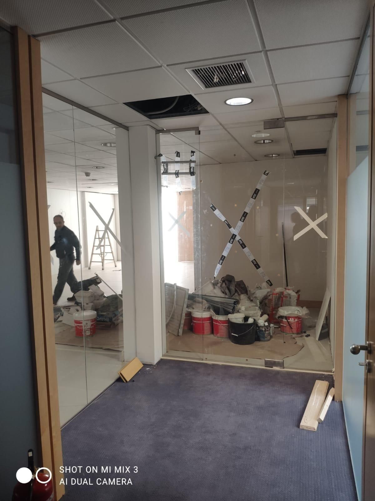 Pasillo de oficina en obras con cristales reparados con cinta adhesiva, latas de pintura y herramientas en el suelo