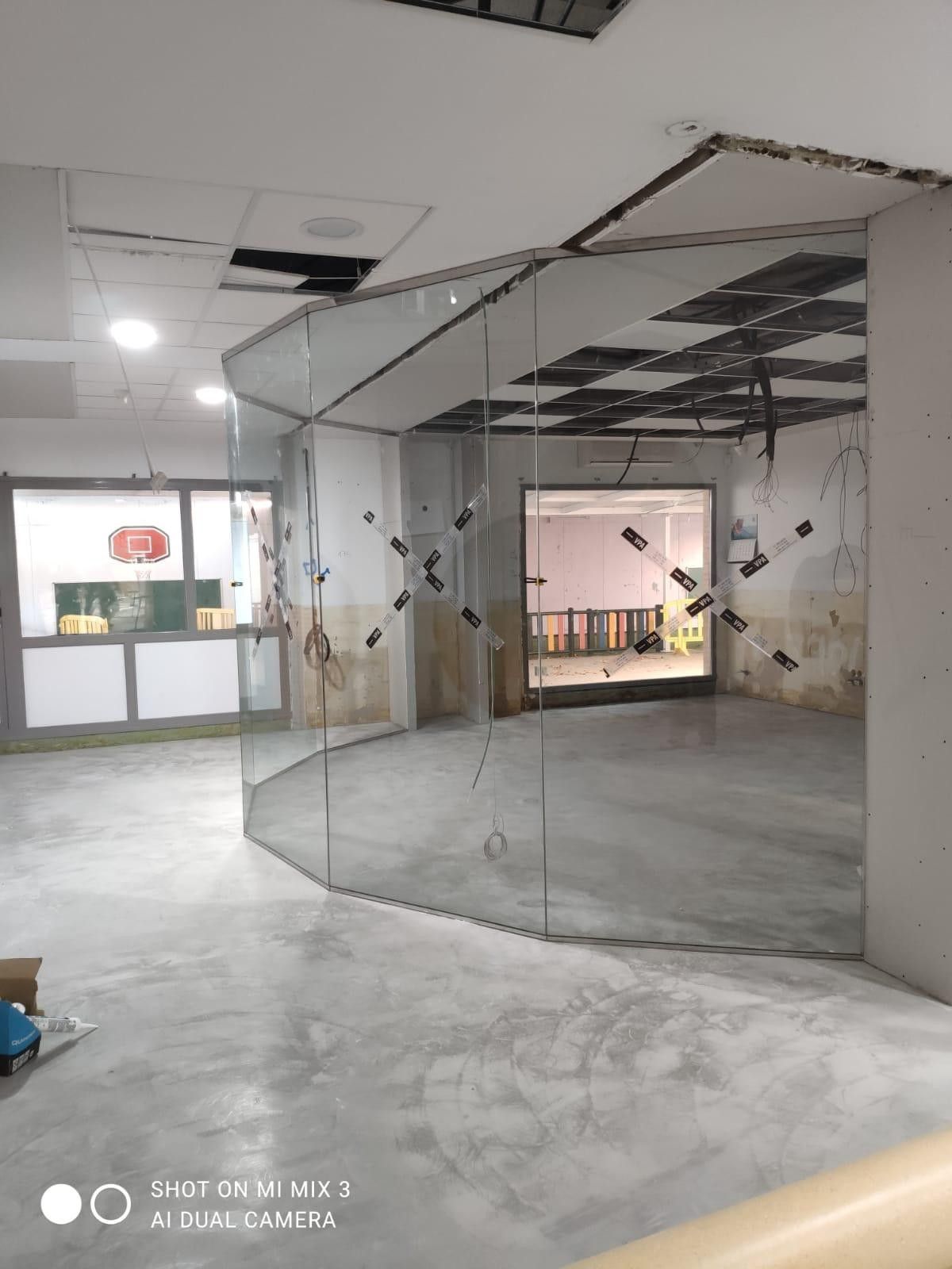 Espacio interior vacío con suelo de hormigón, techo visto y tabiques de cristal en construcción.