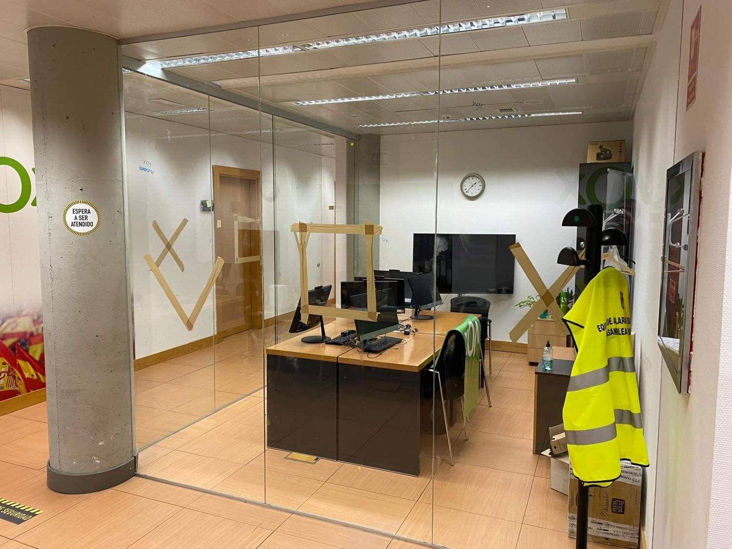 Oficina vacía con escritorios, sillas, una computadora y un chaleco reflectante colgado en un perchero.