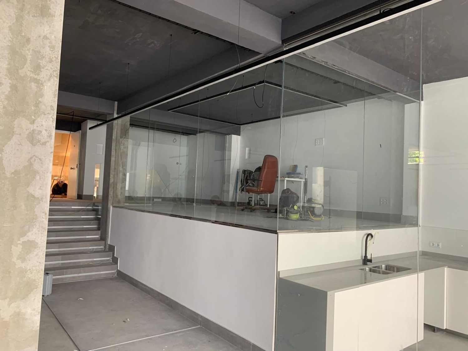Interior moderno con oficina con paredes de vidrio, escaleras y cocina pequeña en construcción.