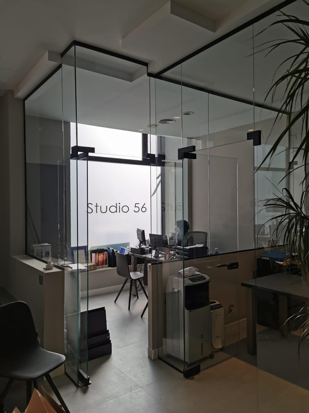 Entrada a la oficina con paredes de cristal, escritorios, sillas y un letrero de 