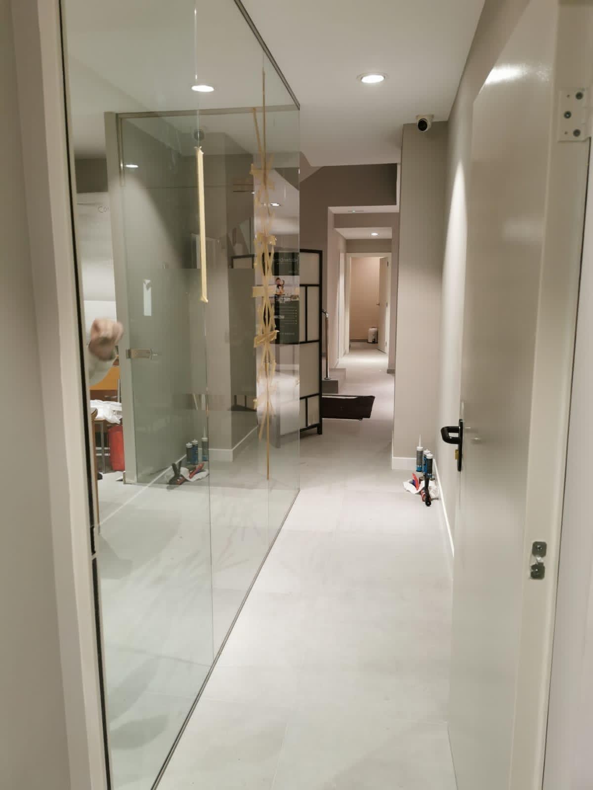 Estrecho pasillo moderno con paredes de cristal, suelos blancos y puertas que dan a las habitaciones.