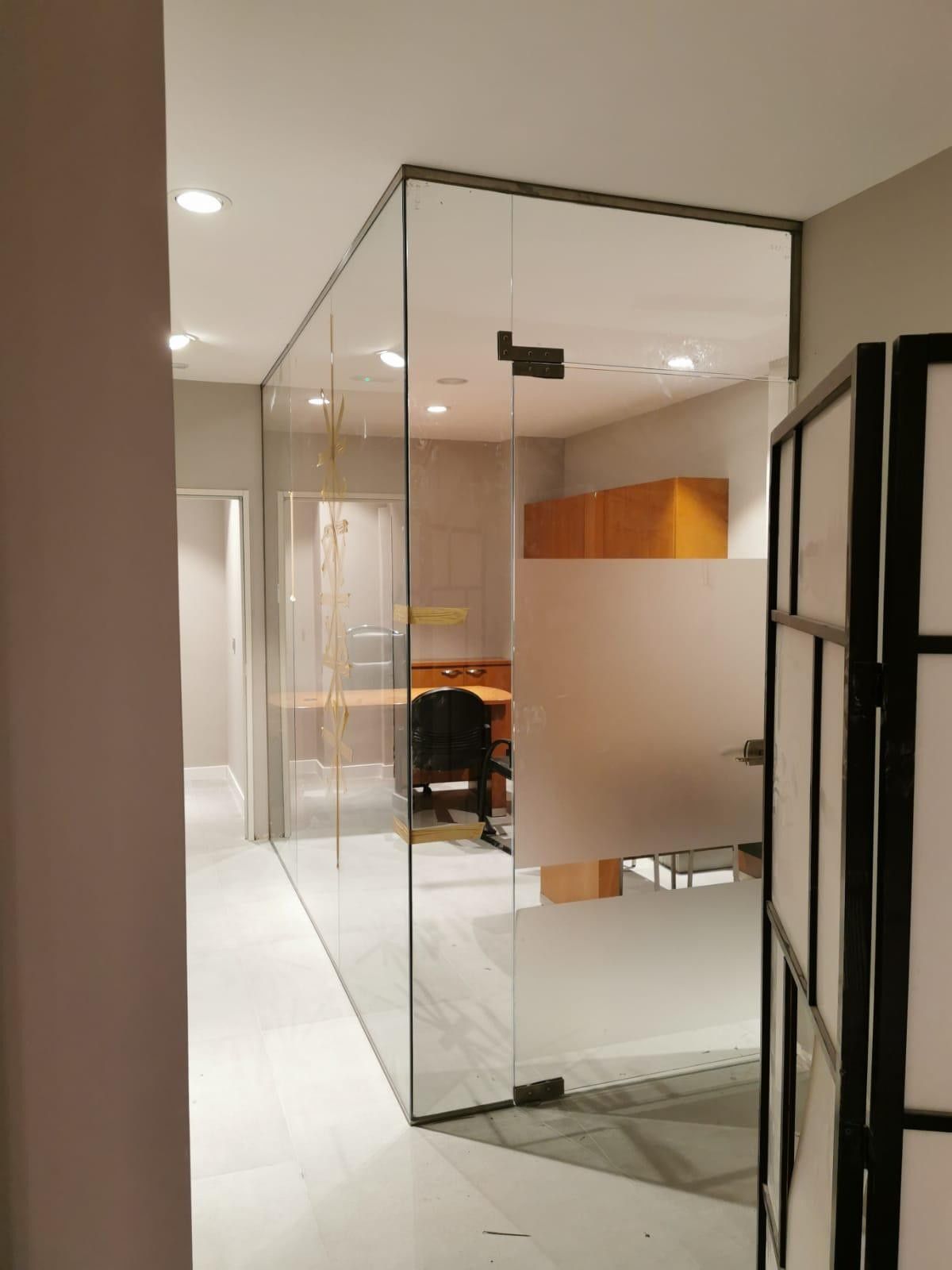 Pasillo de oficina con paredes de cristal, escritorio y armario con marco negro en un interior moderno.