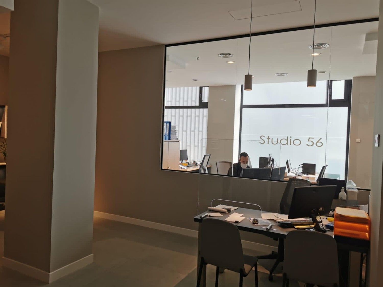 Oficina vacía con escritorios y sillas, vista a través de una gran ventana interior con la etiqueta 