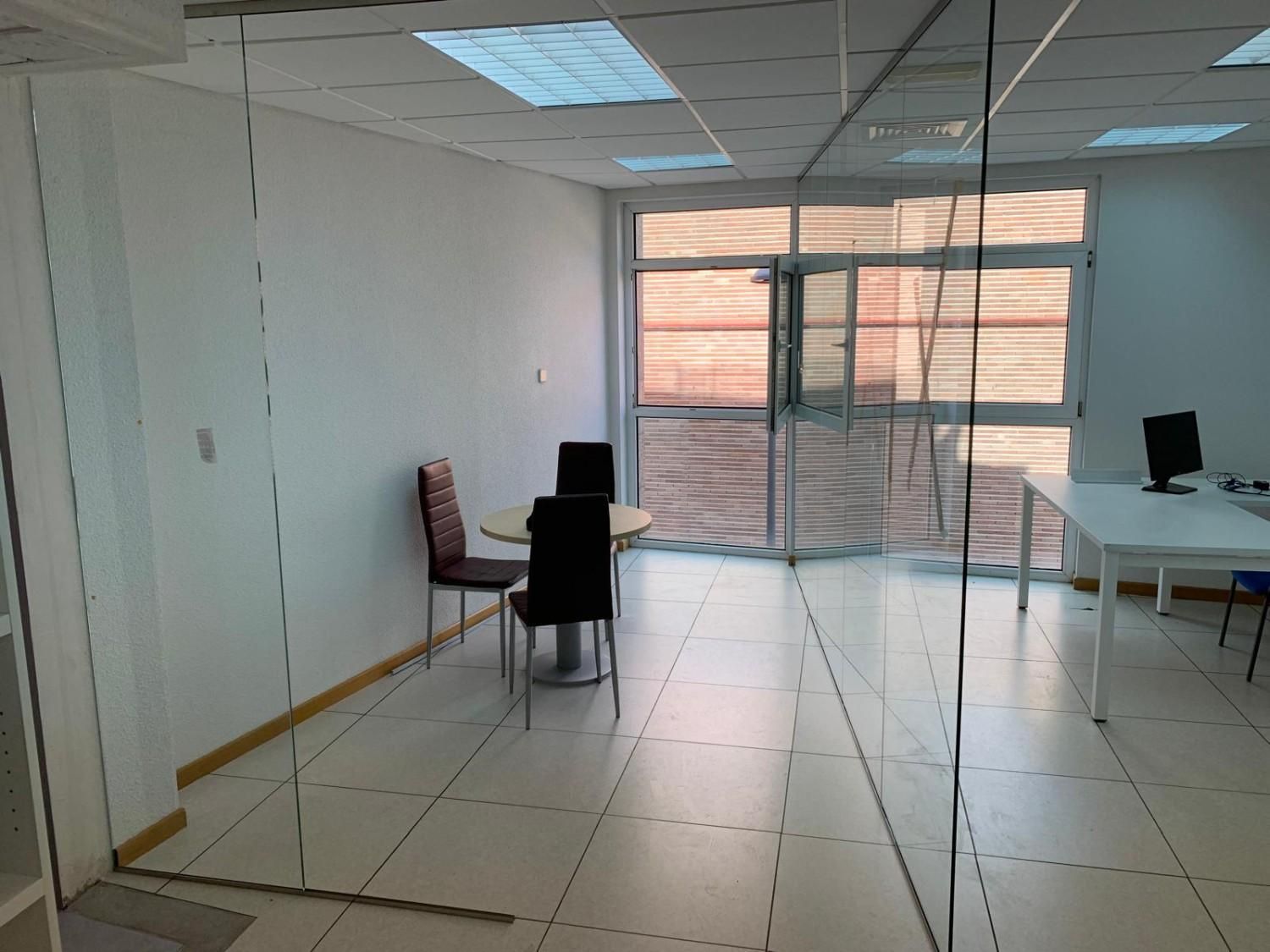 Oficina vacía con suelo de baldosas blancas, dos sillas, un escritorio y puertas de cristal con persianas