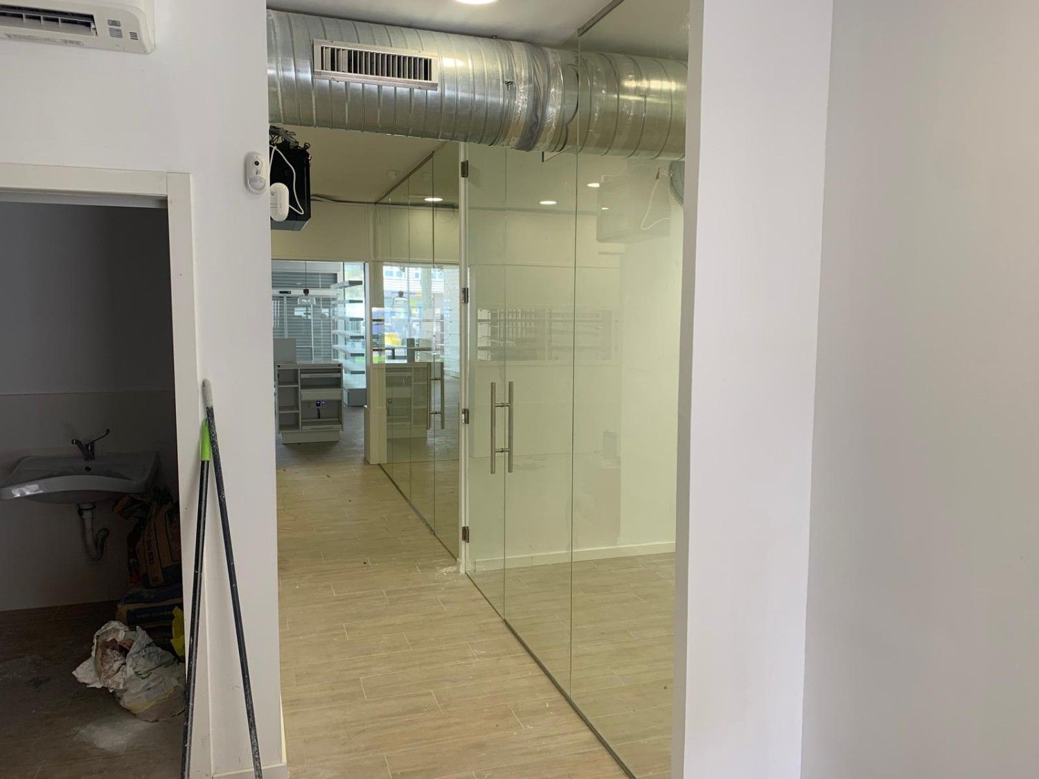 Pasillo de oficina vacío con puertas de cristal, suelo de baldosas y el interior de las habitaciones visible.