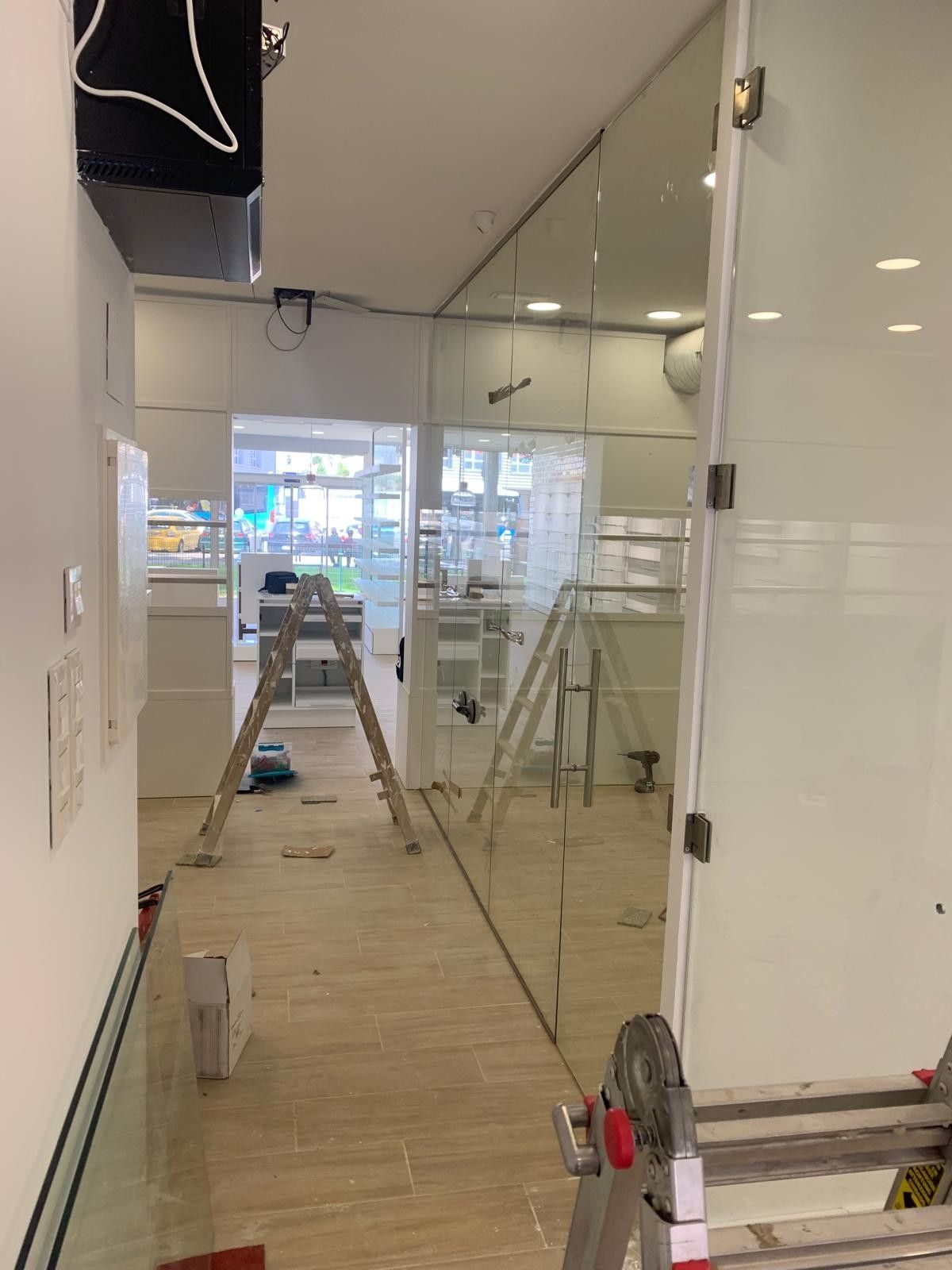 Pasillo interior en obras con pared de cristal, escaleras y herramientas de construcción en el suelo.