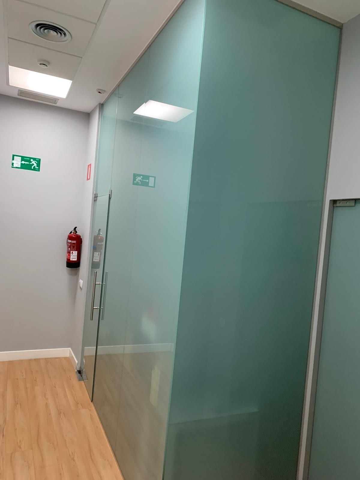 Pasillo de oficina con mampara de vidrio esmerilado, suelo de madera, señal de salida