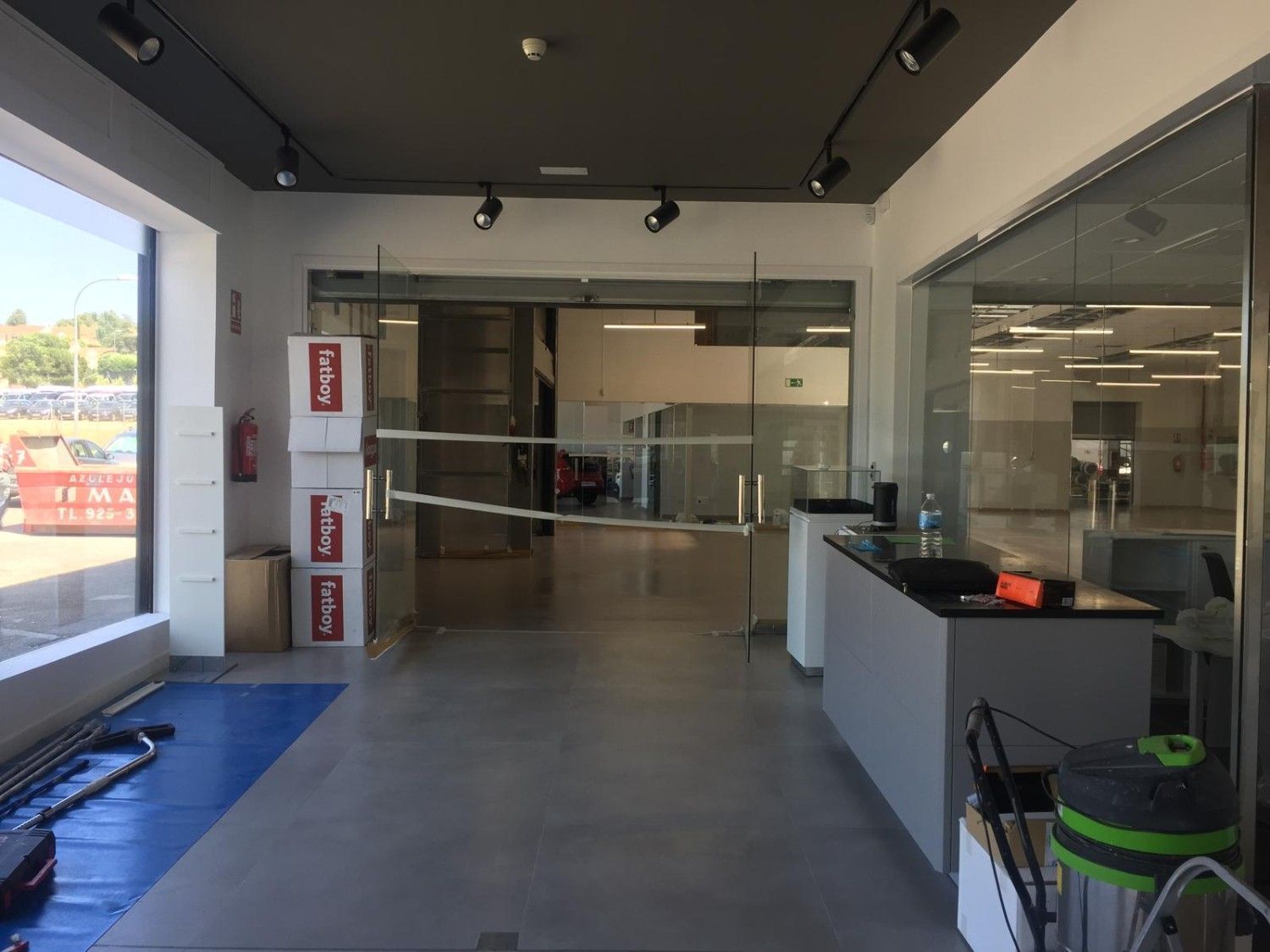 Vestíbulo de oficina vacío con puertas de cristal, suelo gris y productos de limpieza cerca de la entrada.