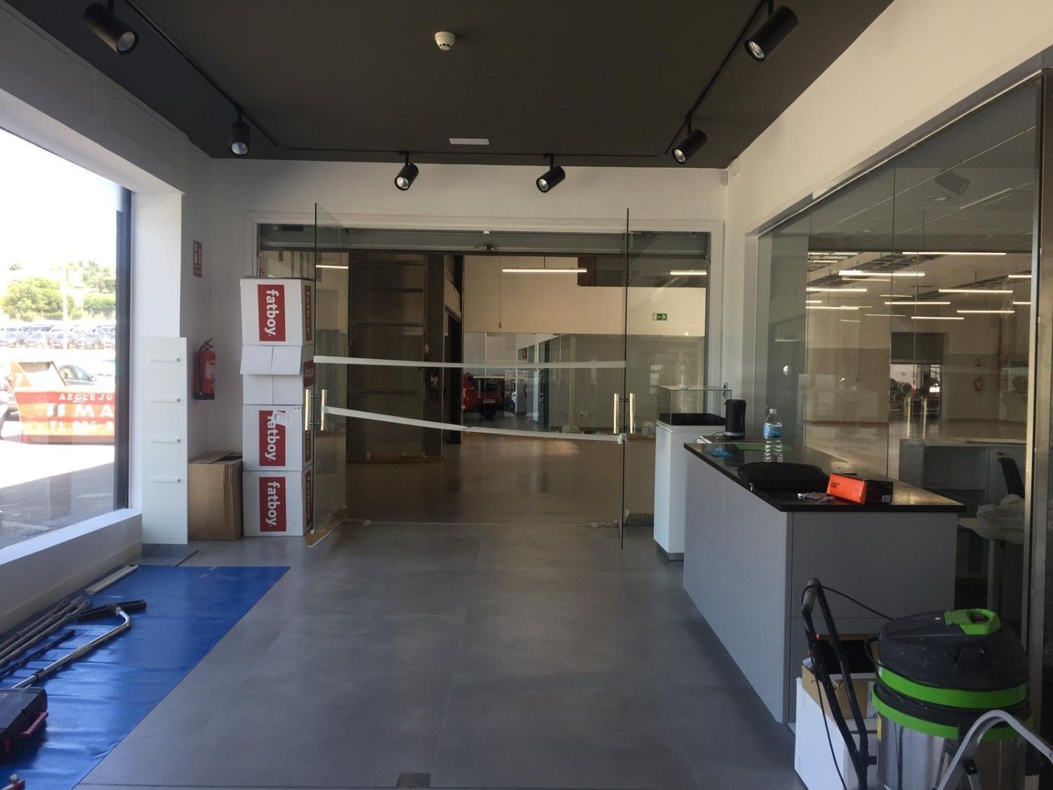 Área de servicio interior vacía con puertas de vidrio, piso gris y un mostrador a la derecha.