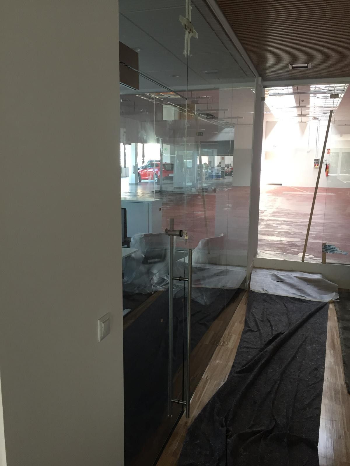 Pasillo con paredes de cristal y suelo cubierto junto a un patio de ladrillo rojo y una luminosa zona exterior.