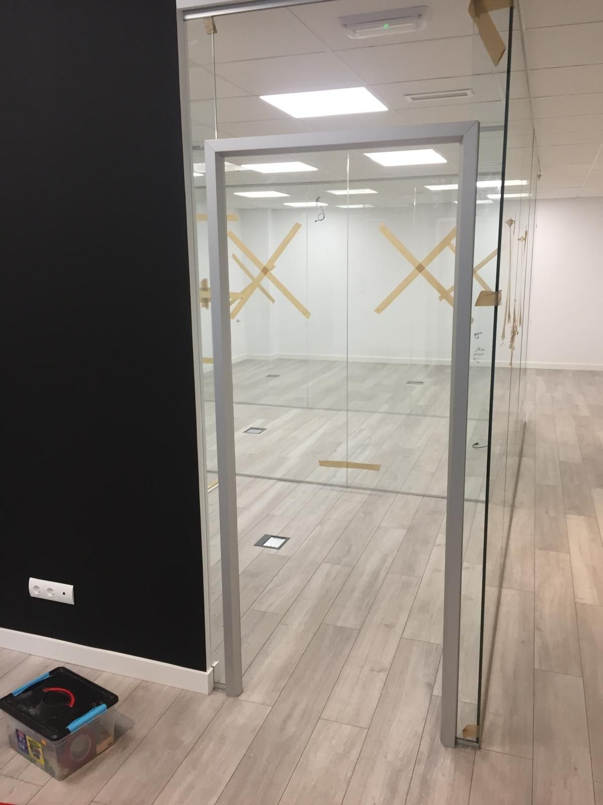 Espacio de oficina vacío con puerta de cristal, pared negra y suelo de madera clara.